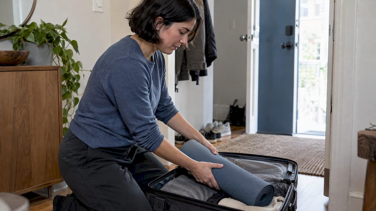 Traveler packing a yoga mat into carry-on luggage