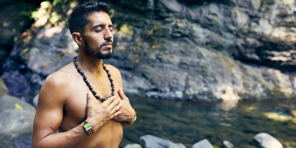 topless man wearing black beaded necklace and blue denim shorts standing on rocky shore during daytime