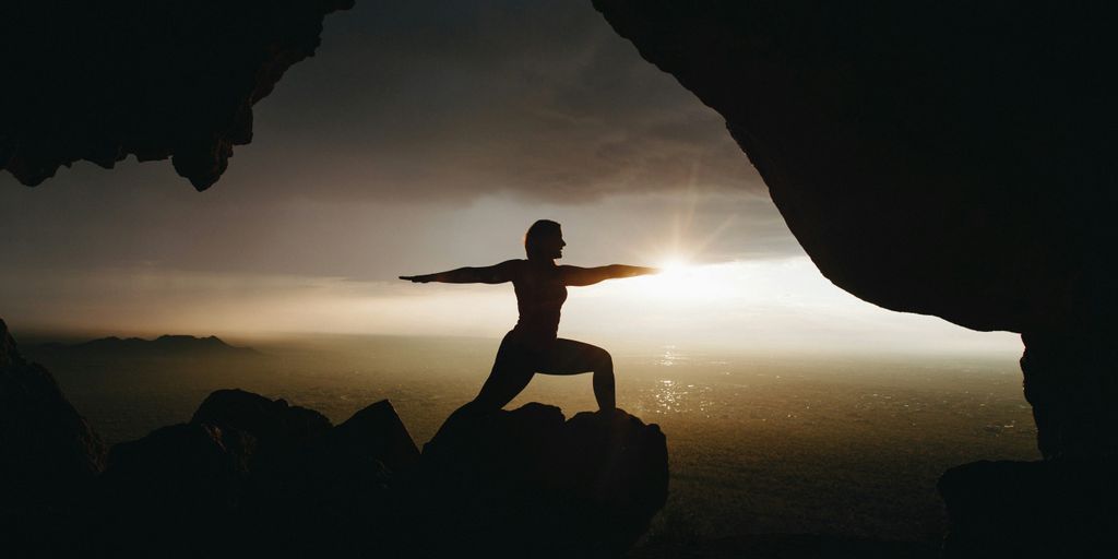 silhouette of person in yoga post on top of cliff during sunset