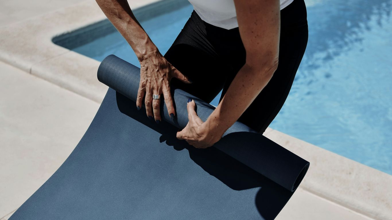 A man holding a yoga mat near a swimming pool