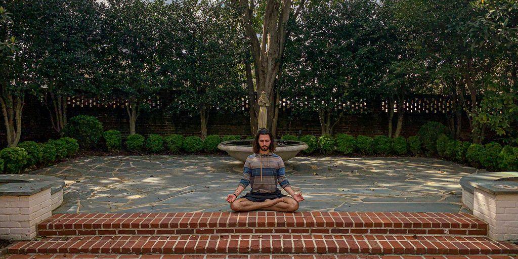 man in blue t-shirt sitting on brown brick floor near green trees during daytime