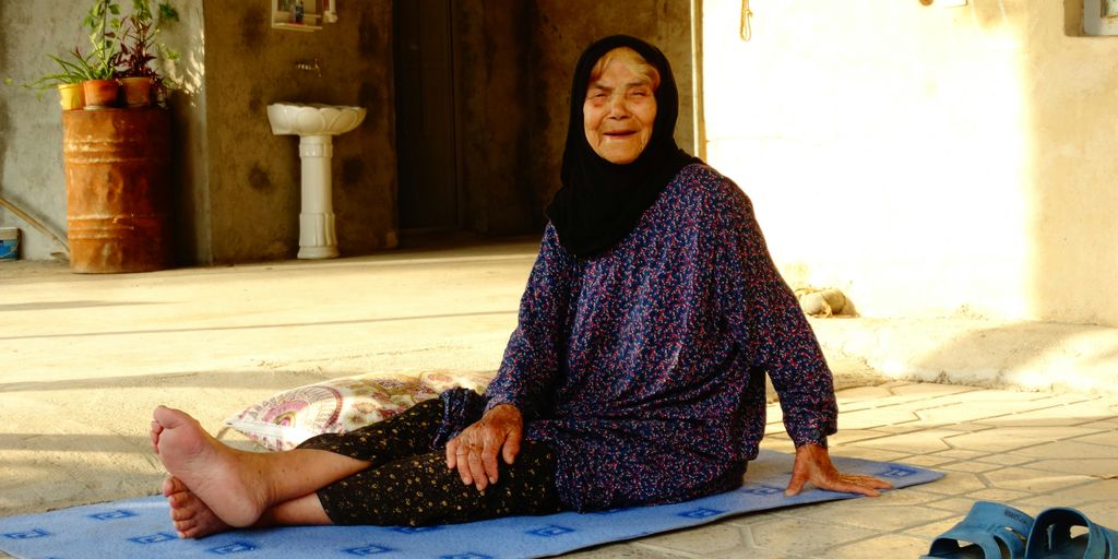 An elderly woman smiles while sitting outside.