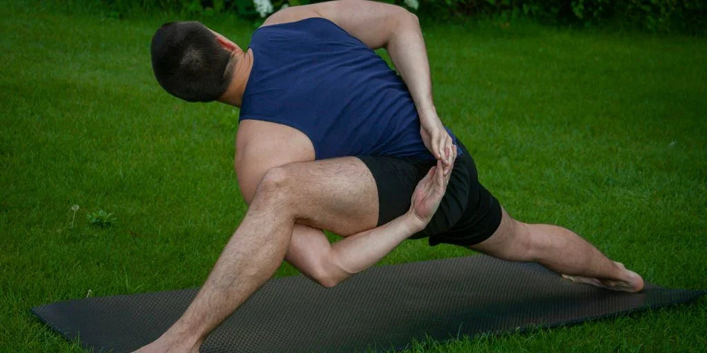 man in blue tank top and black shorts lying on black mat on green grass field