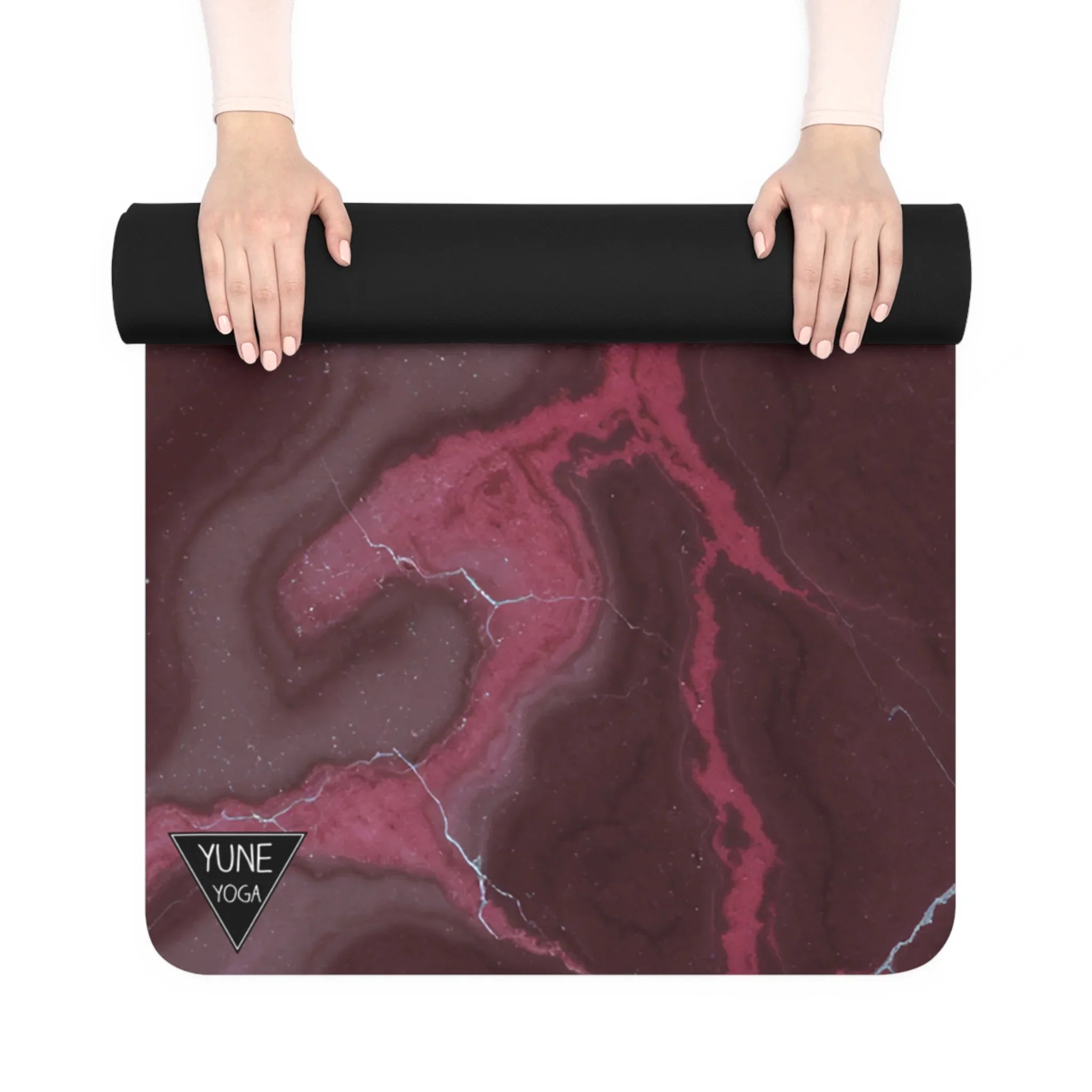 Hands rolling out a pink marble yoga mat with black edges and geometric design