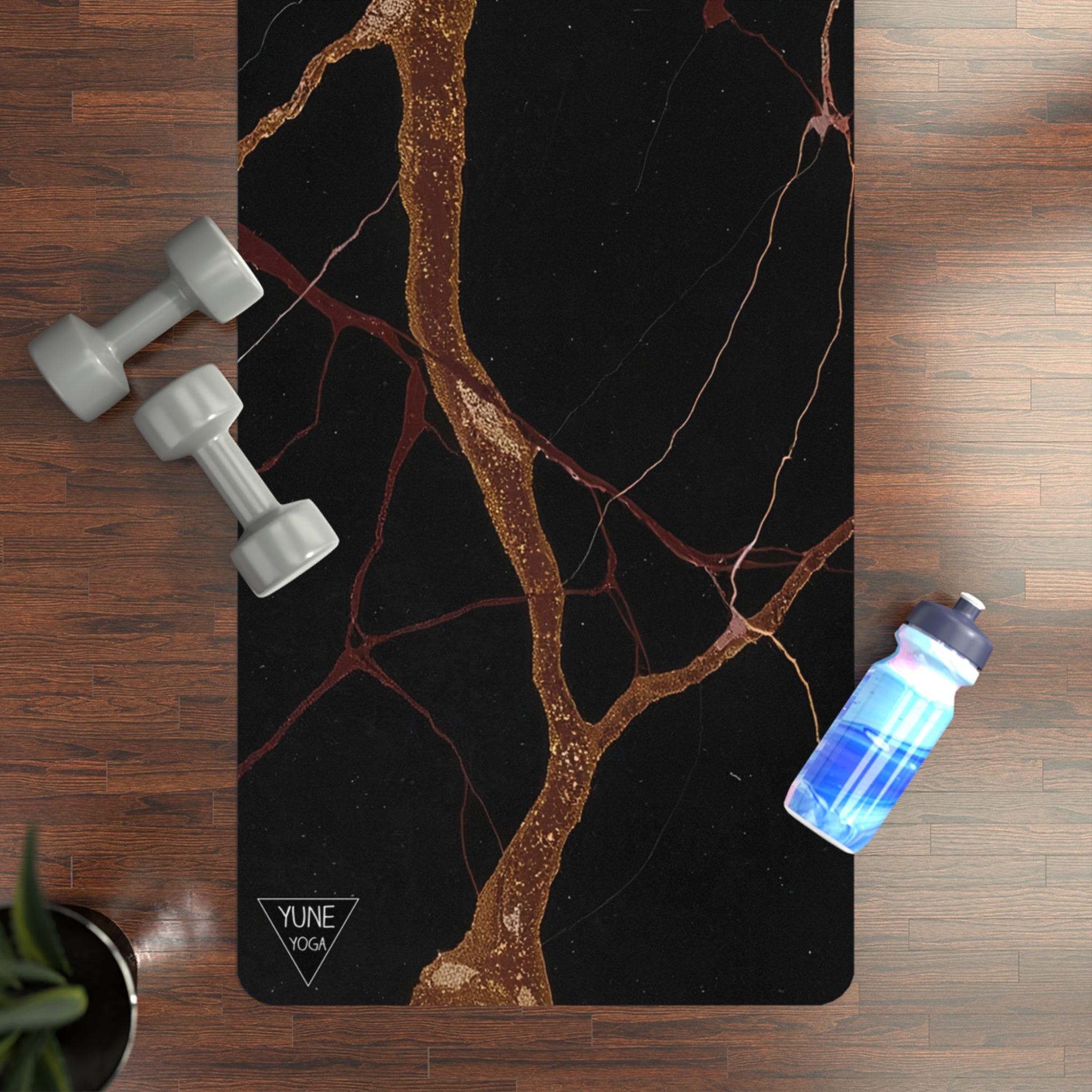 Black marble yoga mat with gold veins, dumbbells, and water bottle on wood floor