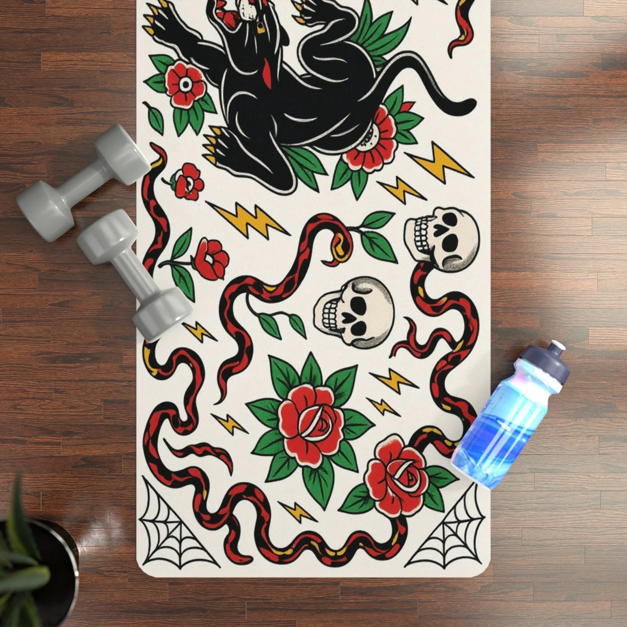 Yoga mat with tattoo-style design on a wooden floor with dumbbells and a water bottle.
