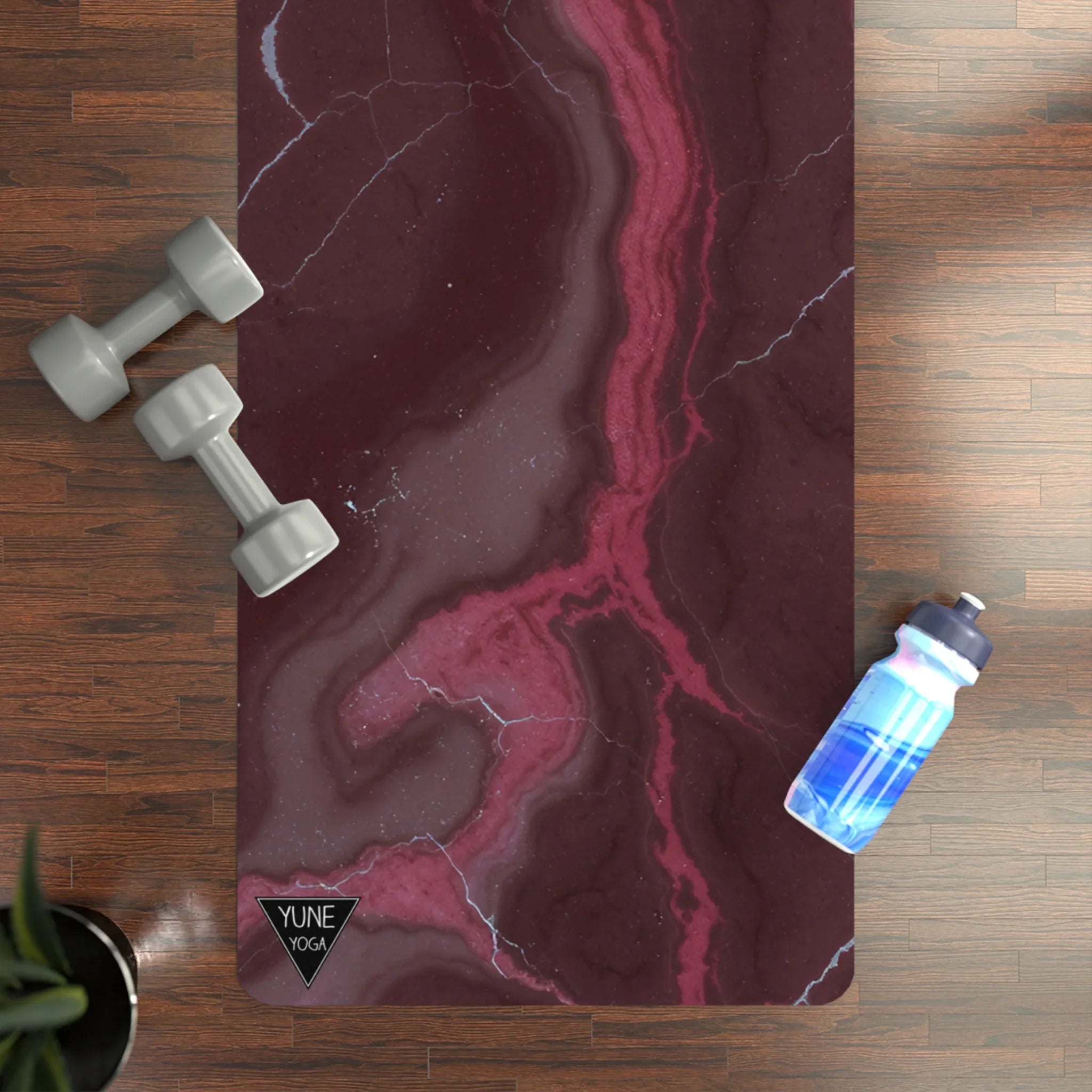Maroon marble yoga mat on wood floor with gray dumbbells and a blue water bottle