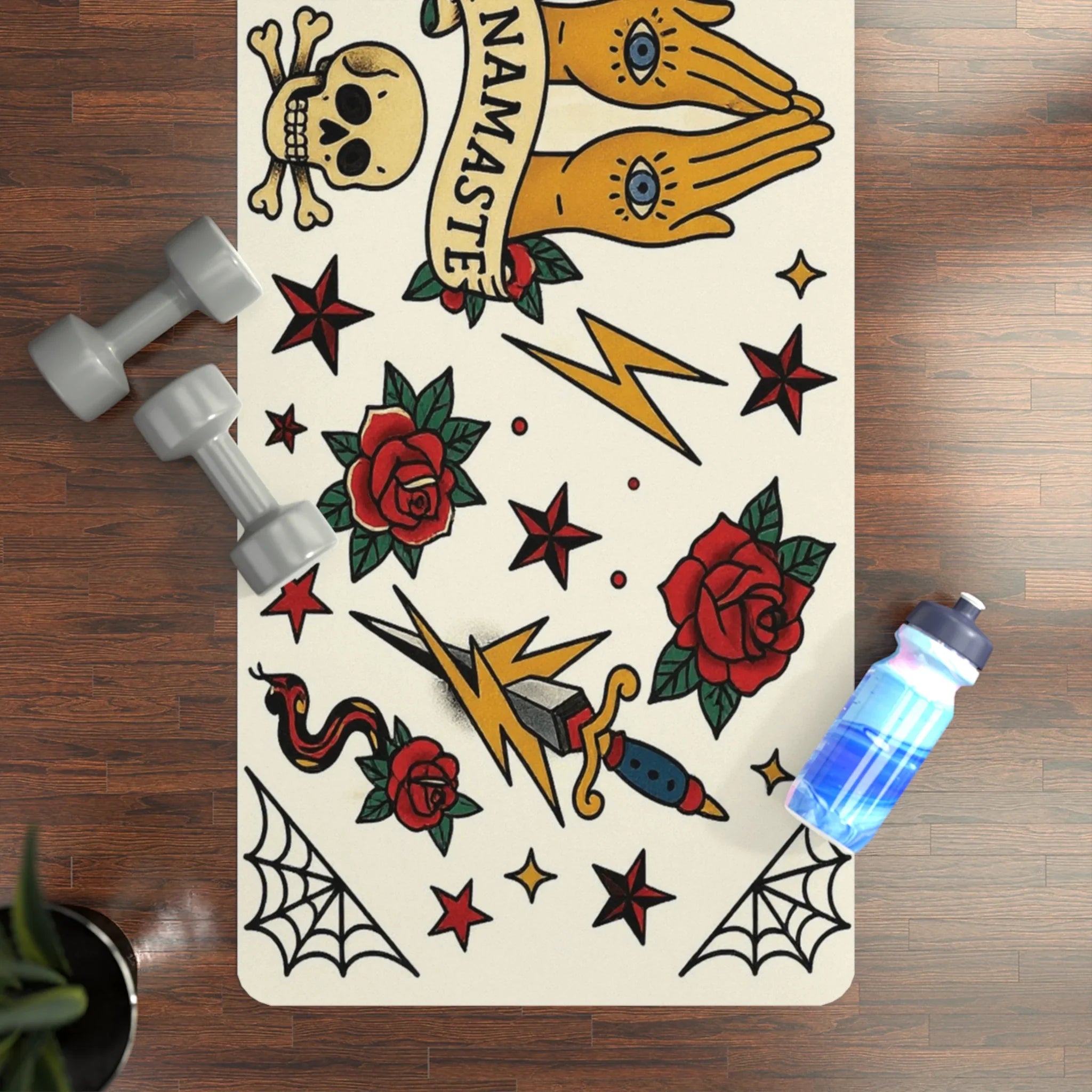 Yoga mat with tattoo designs on a wooden floor with dumbbells and a water bottle.