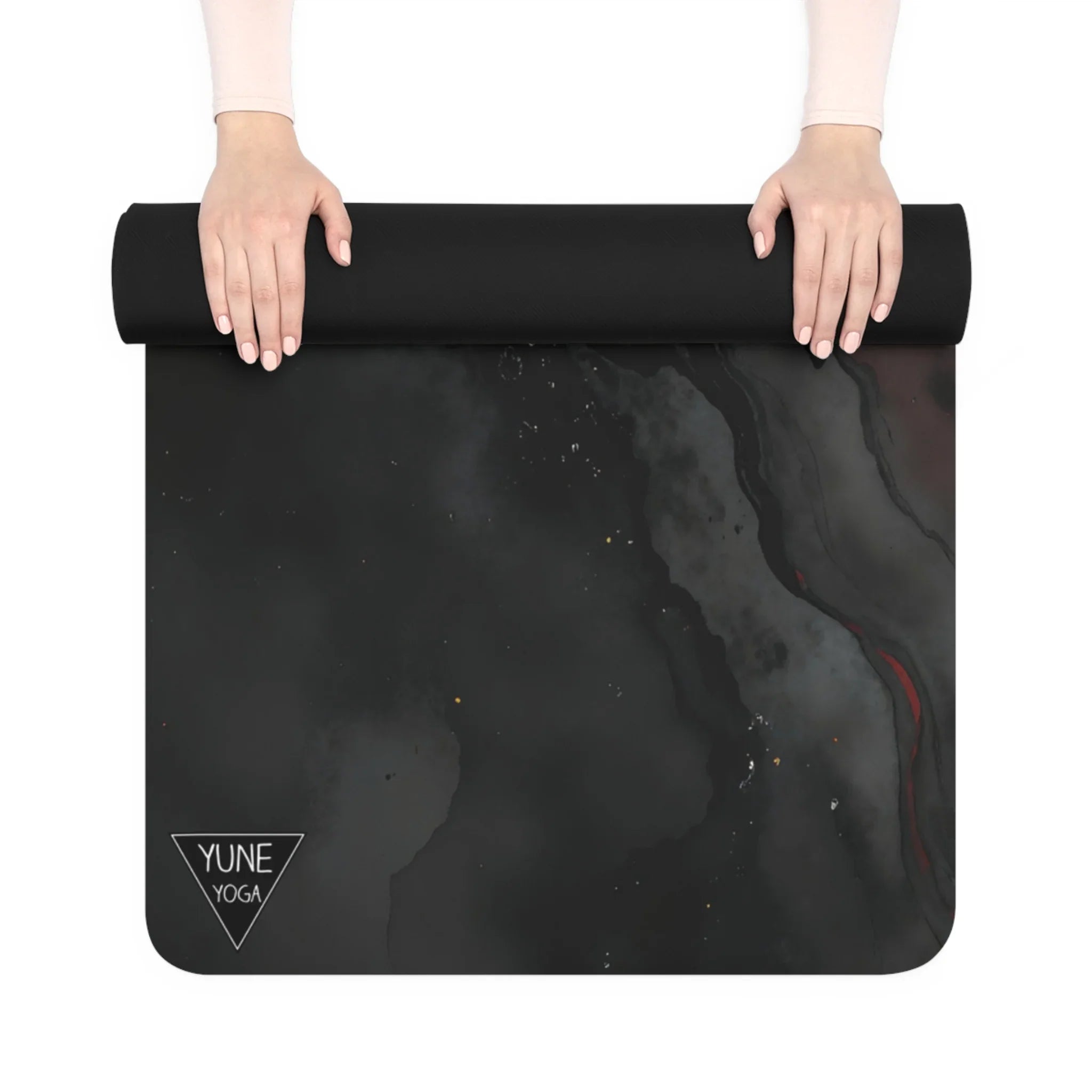 Hands rolling out a black marbled yoga mat with minimalist design and YUNE YOGA logo in the corner.