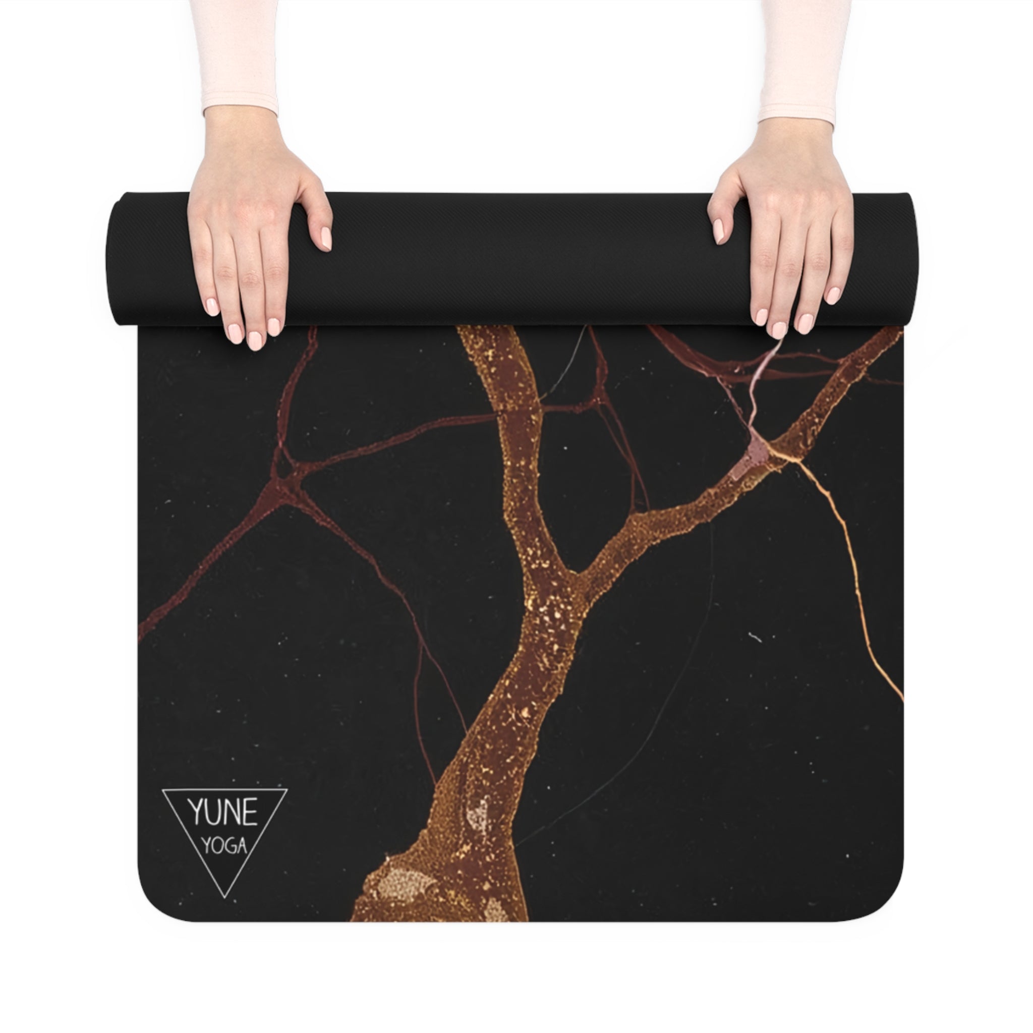 Hands rolling out a black yoga mat with a gold marble pattern on a white surface