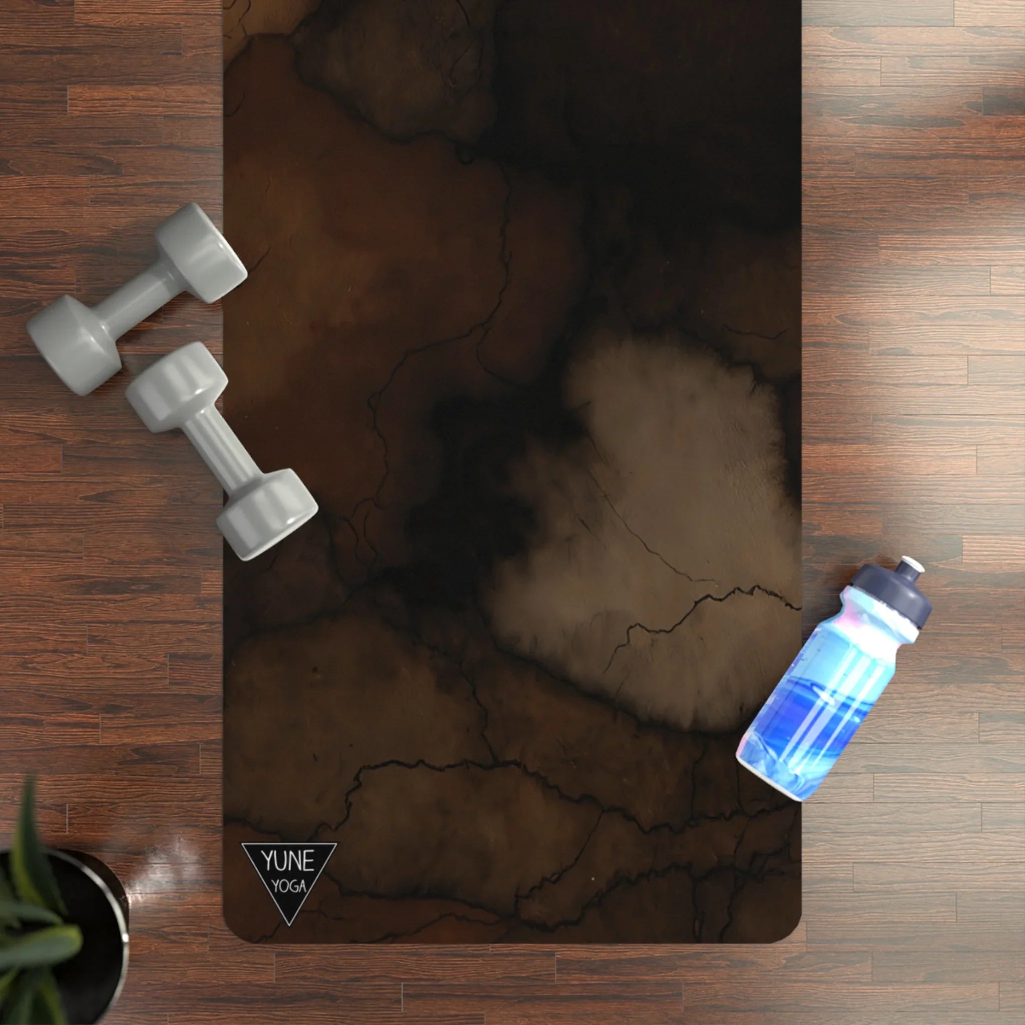 Marbled brown yoga mat on wood floor with dumbbells and water bottle nearby