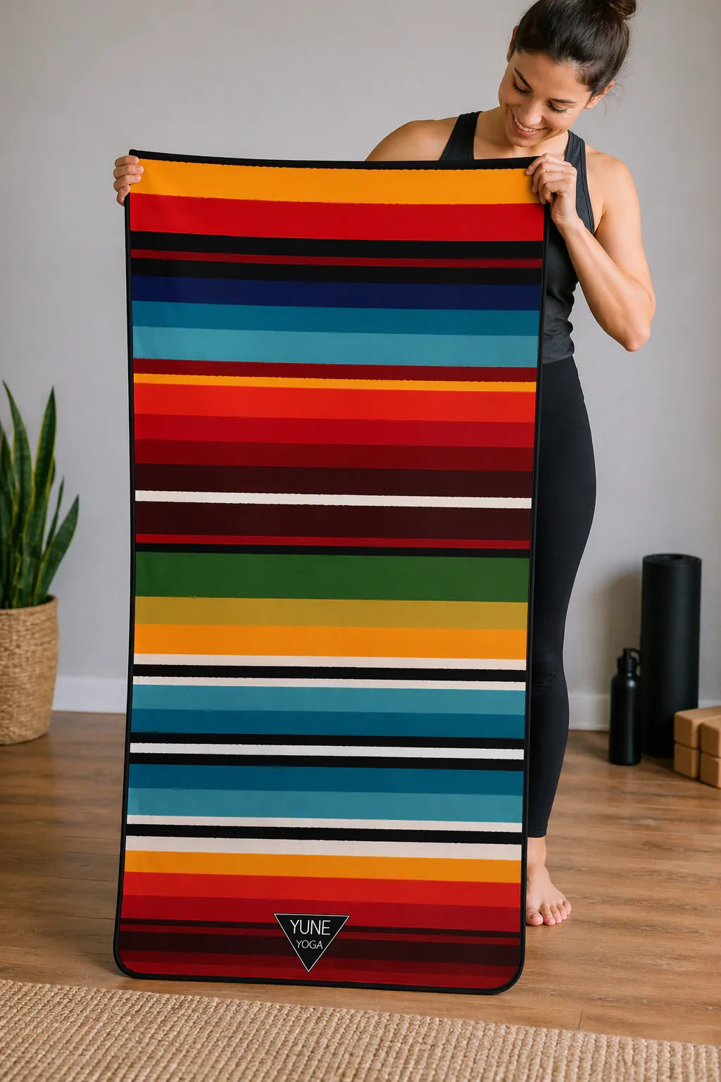Woman holding colorful striped yoga mat in cozy home studio with plant and yoga props