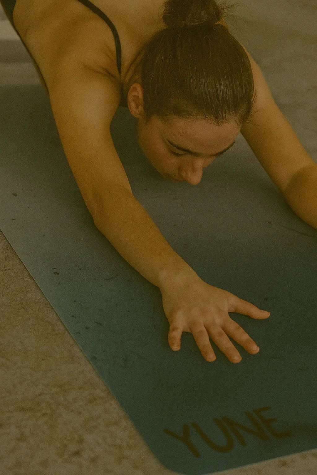 Person on a yoga mat with 'YUNE' branding in a dimly lit setting