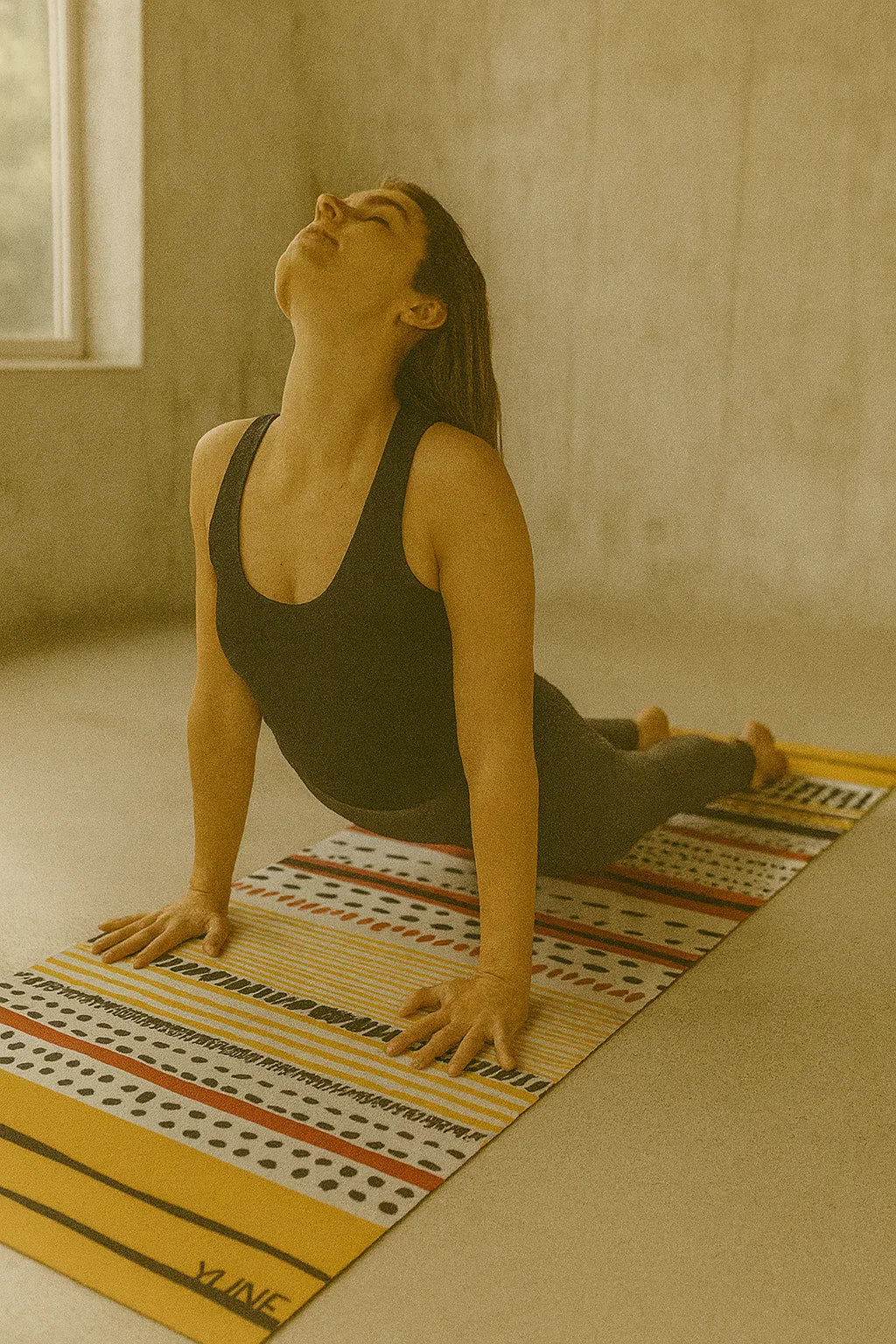 Woman practicing yoga on a striped mat in a room with a window.