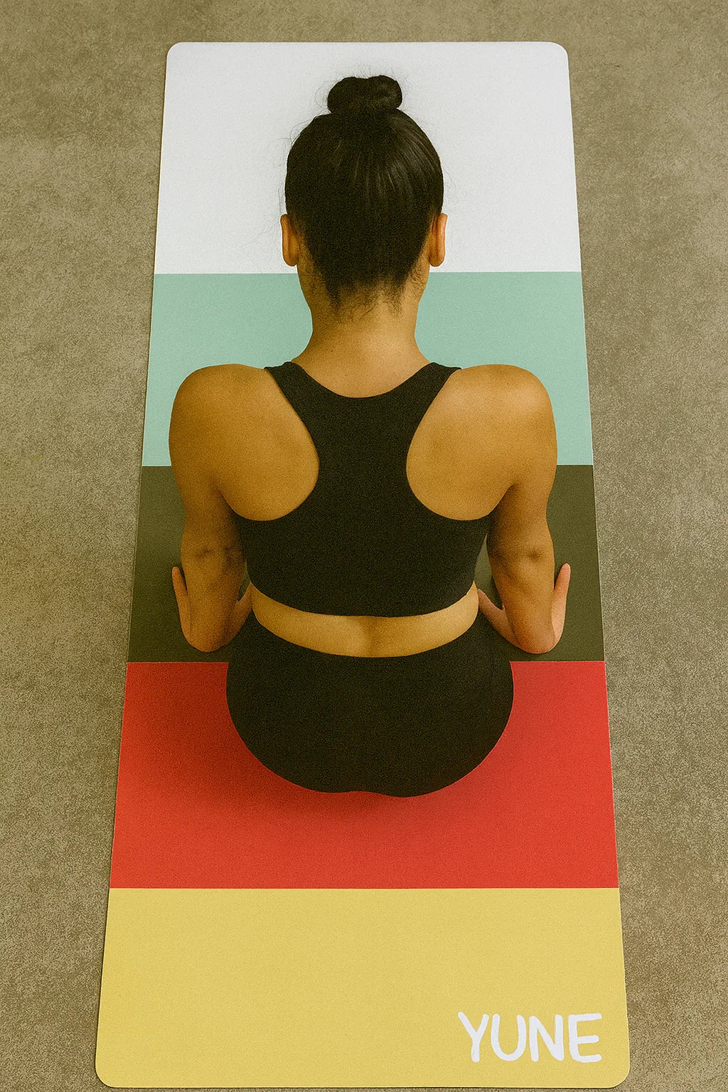 Person sitting on a colorful yoga mat with 'YUNE' branding
