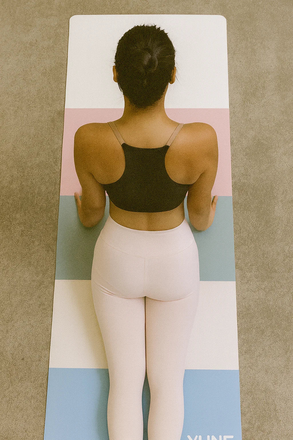 Person wearing a black sports bra and light pink leggings on a colorful yoga mat.