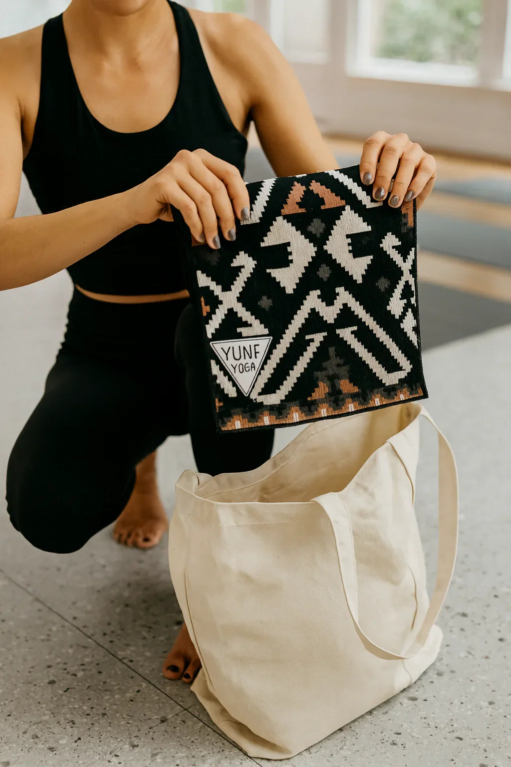 Person holding a patterned bag with 'YUNE' branding next to a beige tote bag.