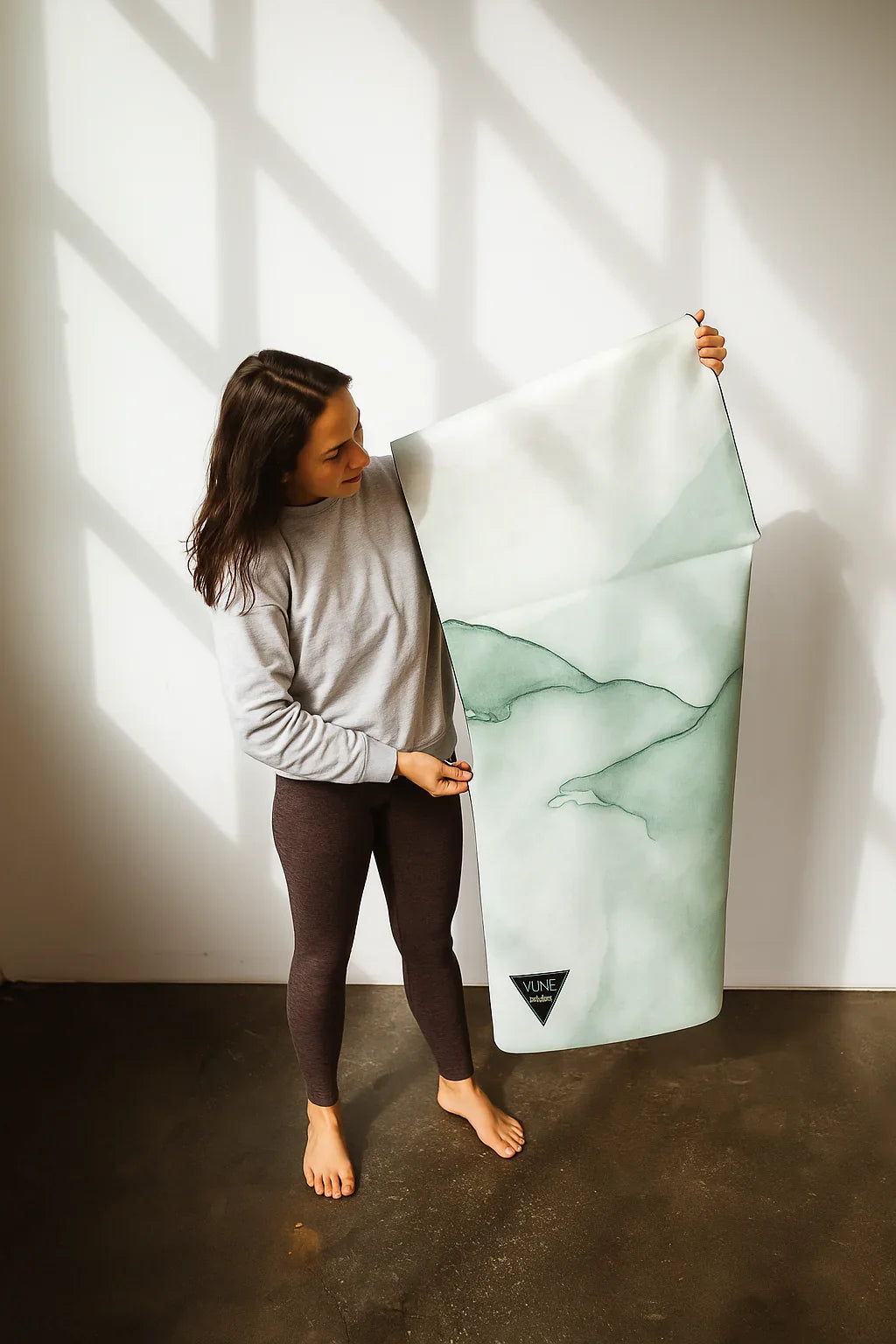 Woman holding a green and white patterned yoga mat in a well-lit room.