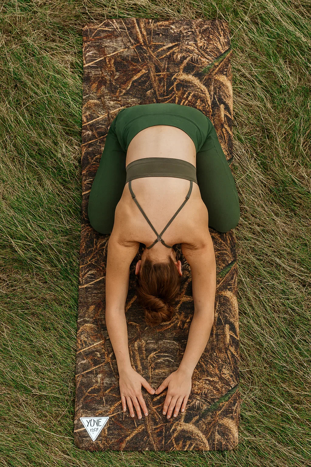 Person lying on a camouflage yoga mat in grass
