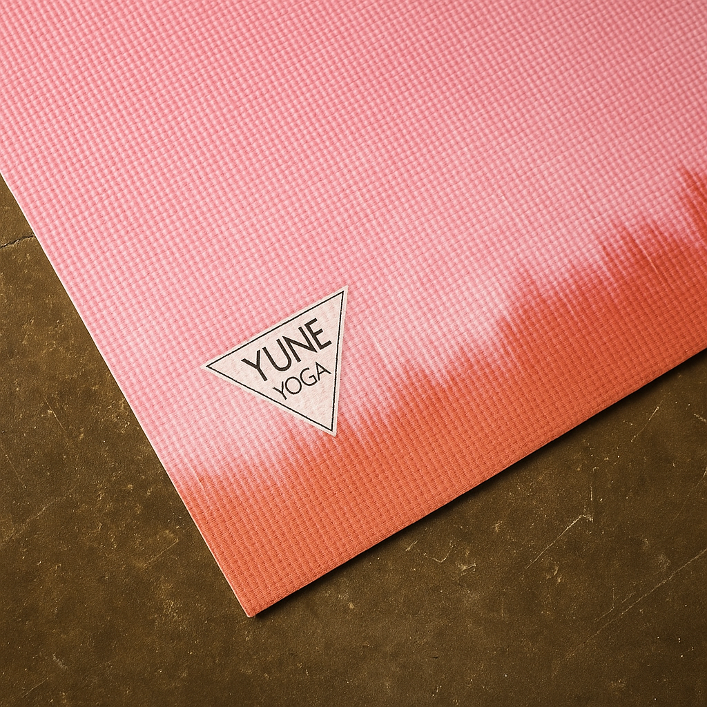 Pink and red gradient yoga mat with YUNE YOGA logo on a brown surface