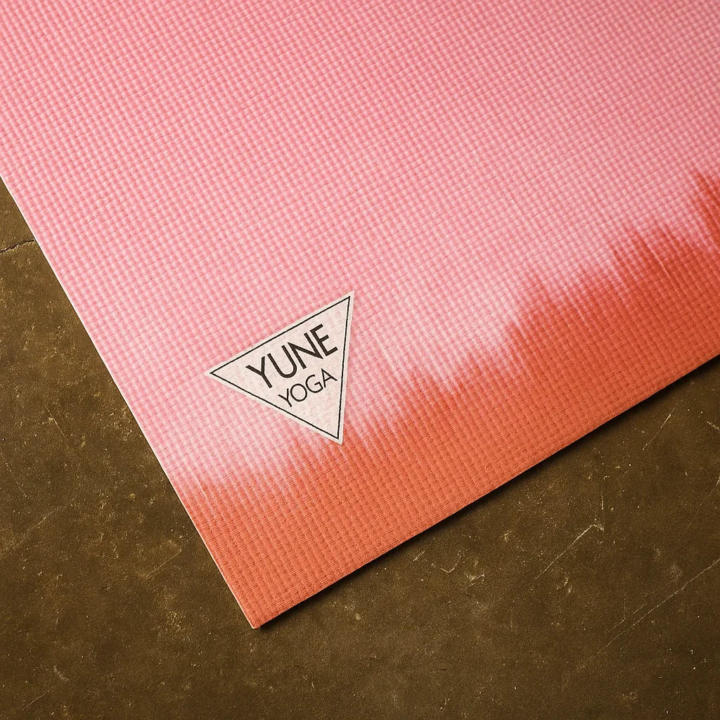 Pink and red gradient yoga mat with YUNE YOGA logo on a brown surface