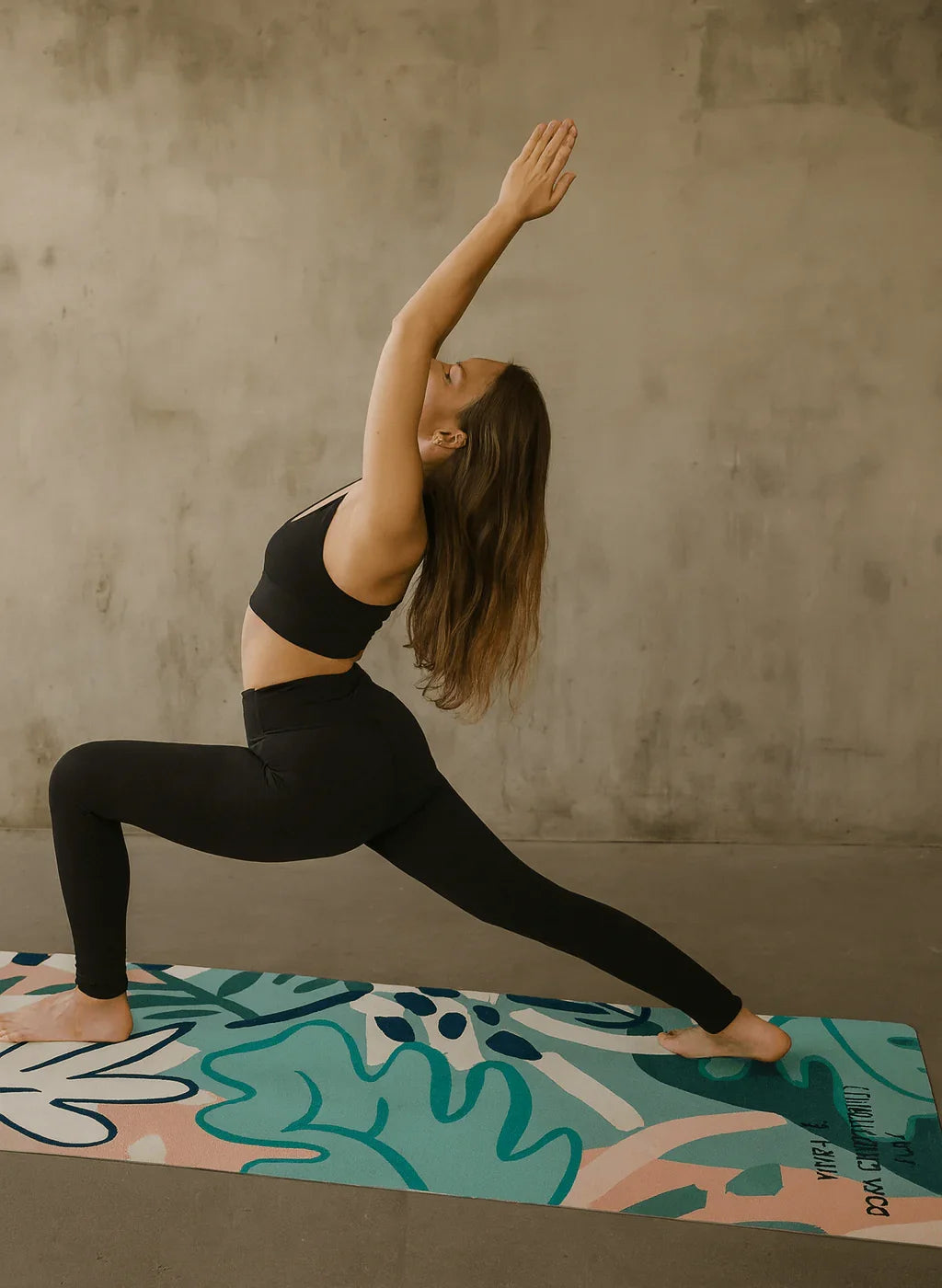 Woman practicing yoga on a colorful mat against a plain wall