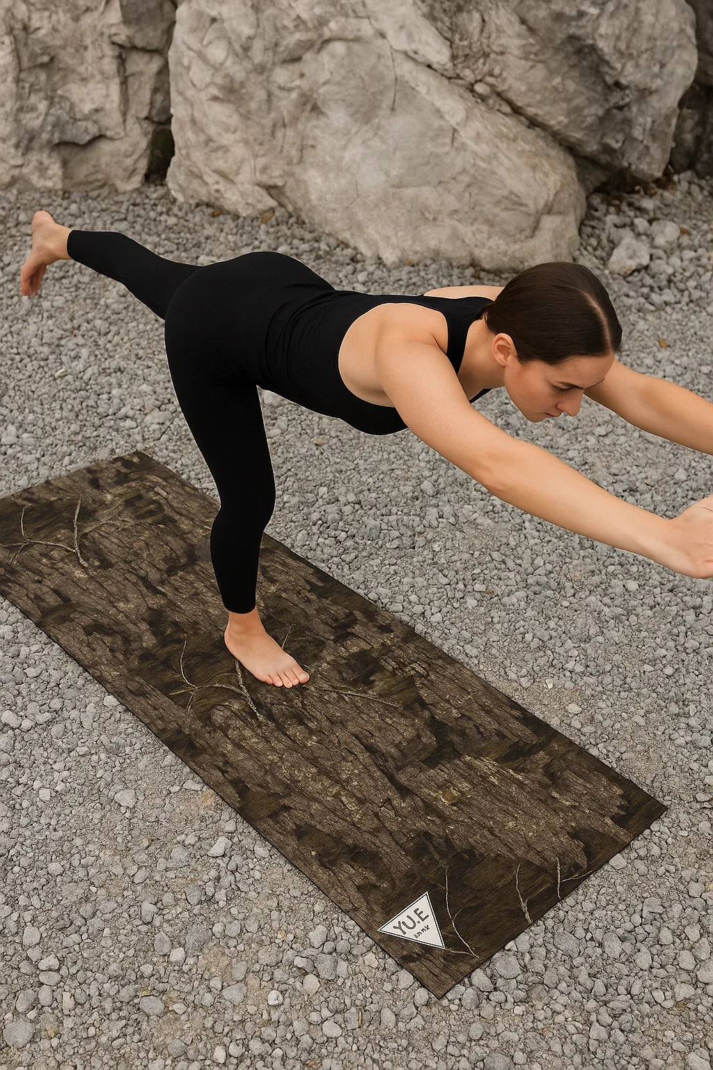 Person practicing yoga on a textured mat outdoors with rocks in the background