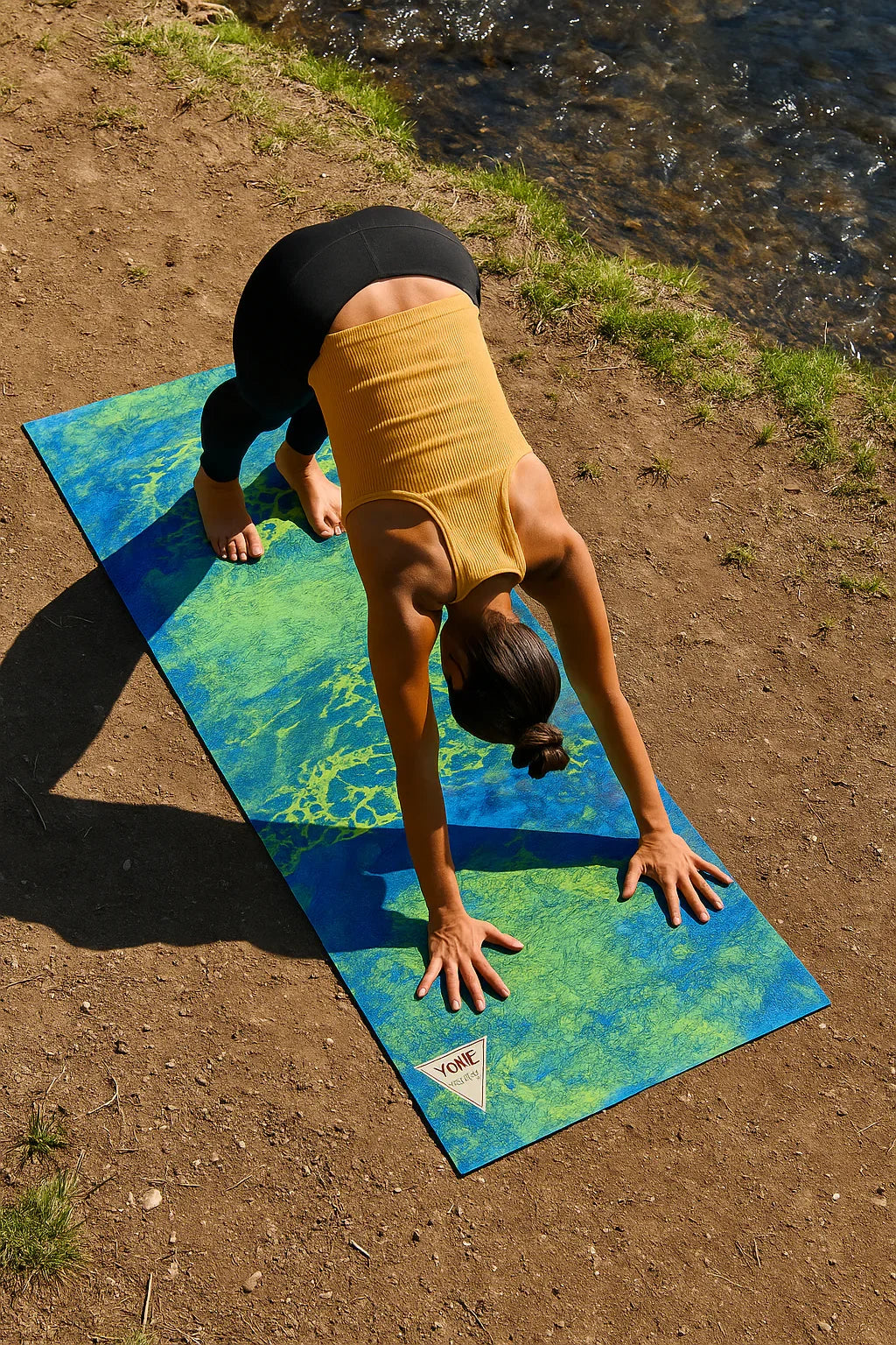 Person doing a handstand on a colorful yoga mat by a body of water.
