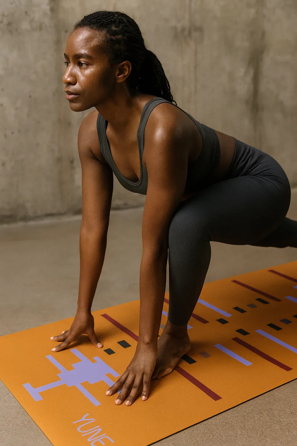 Person in athletic wear on an orange yoga mat with a geometric design against a concrete wall.