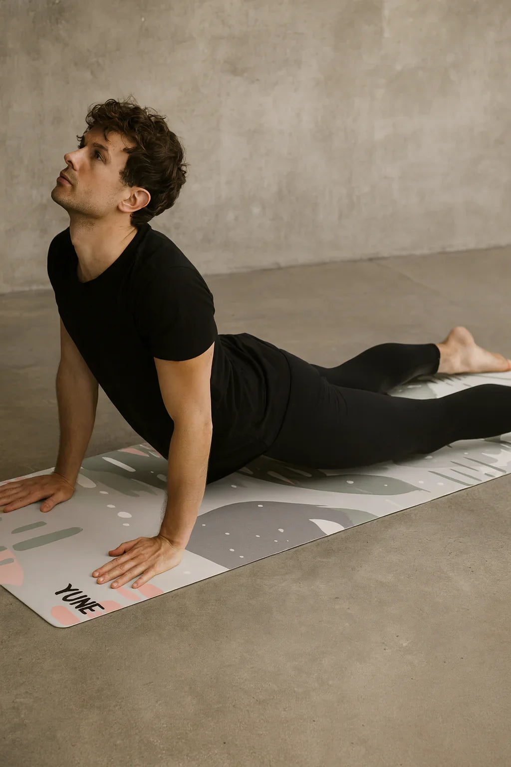 Person in a black outfit performing a yoga pose on a branded mat against a neutral background