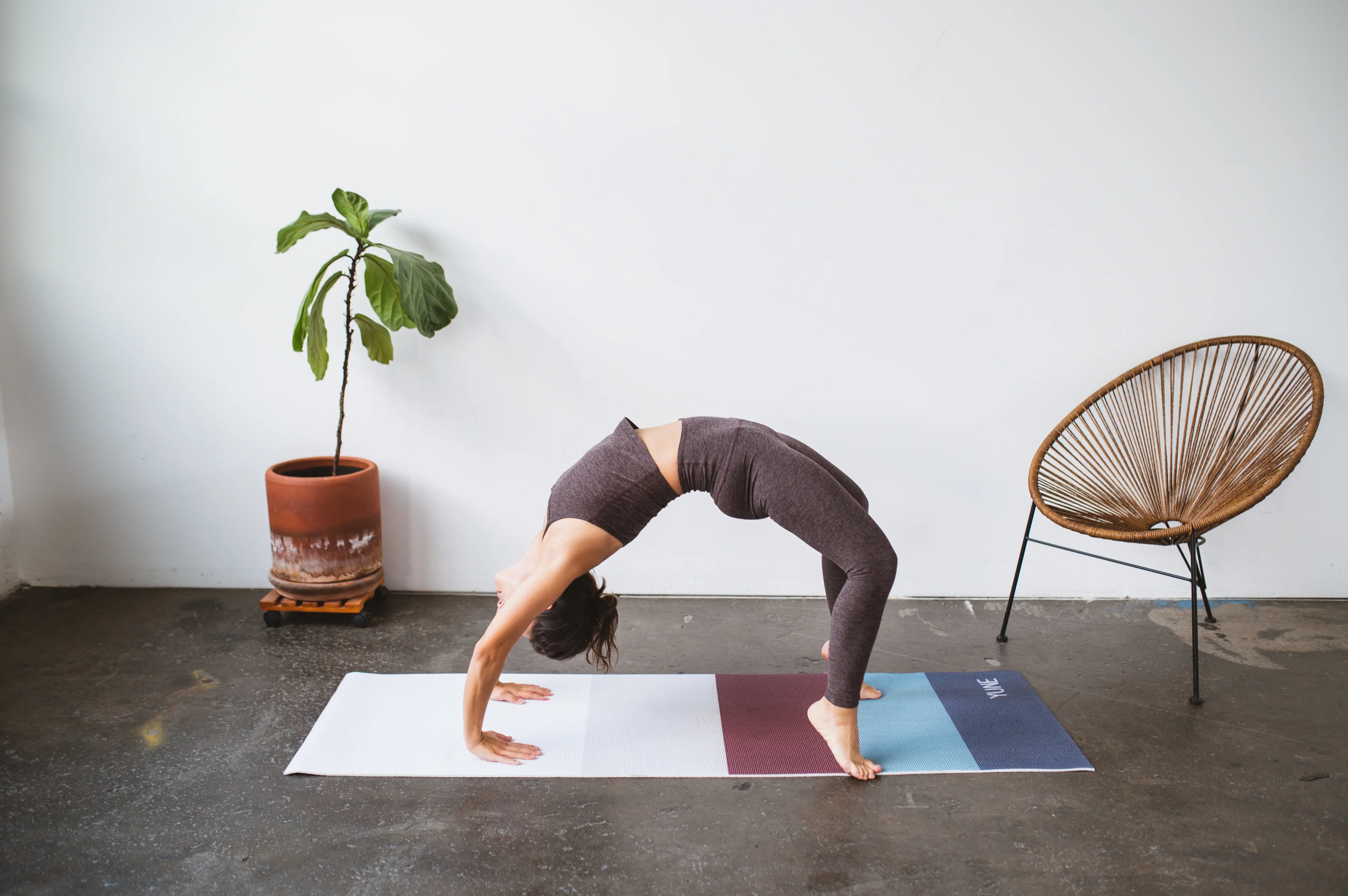 Person performing a yoga pose on a mat with a plant and chair in the background