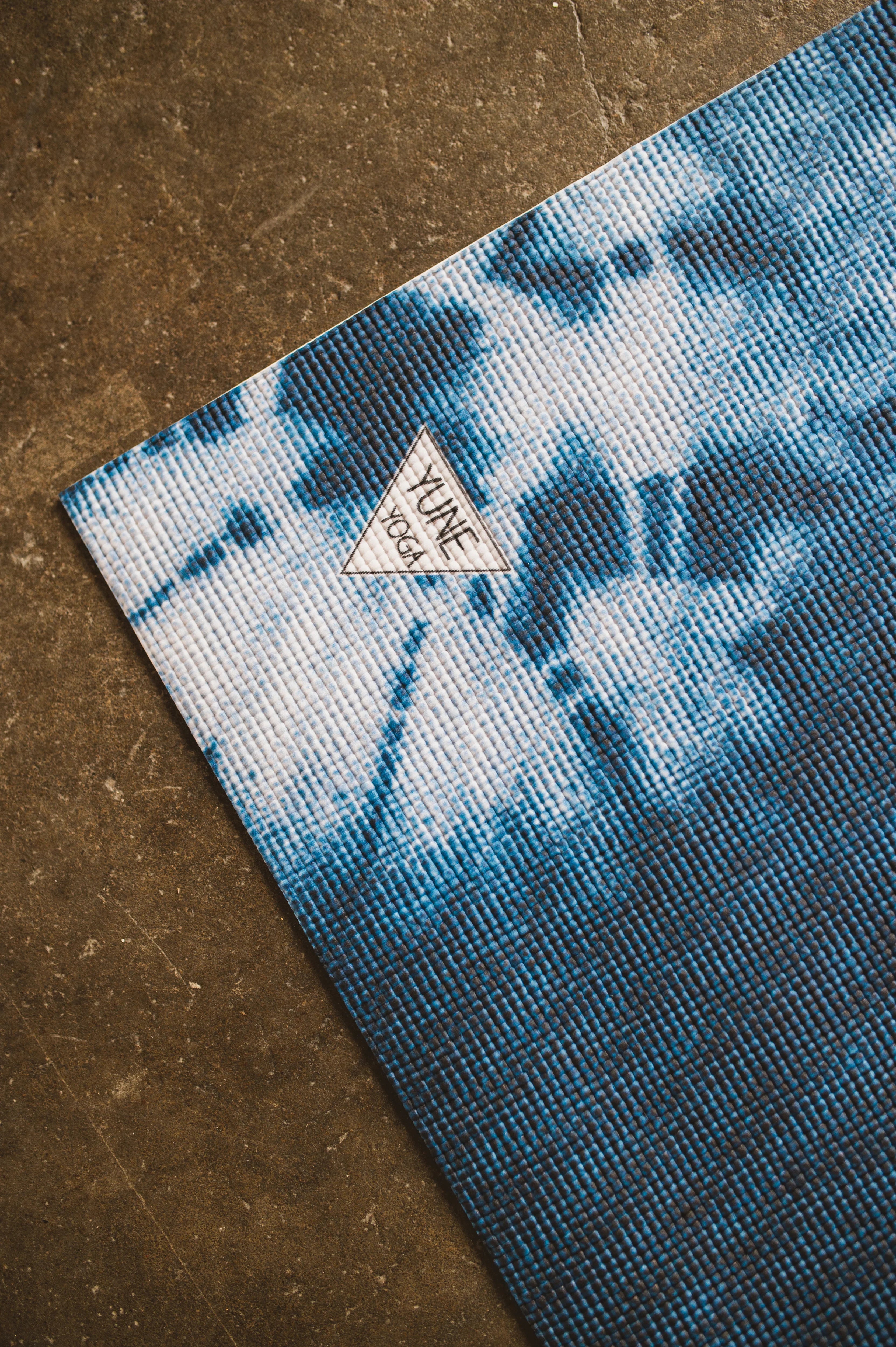 Blue tie-dye yoga mat with a brand logo on a brown surface