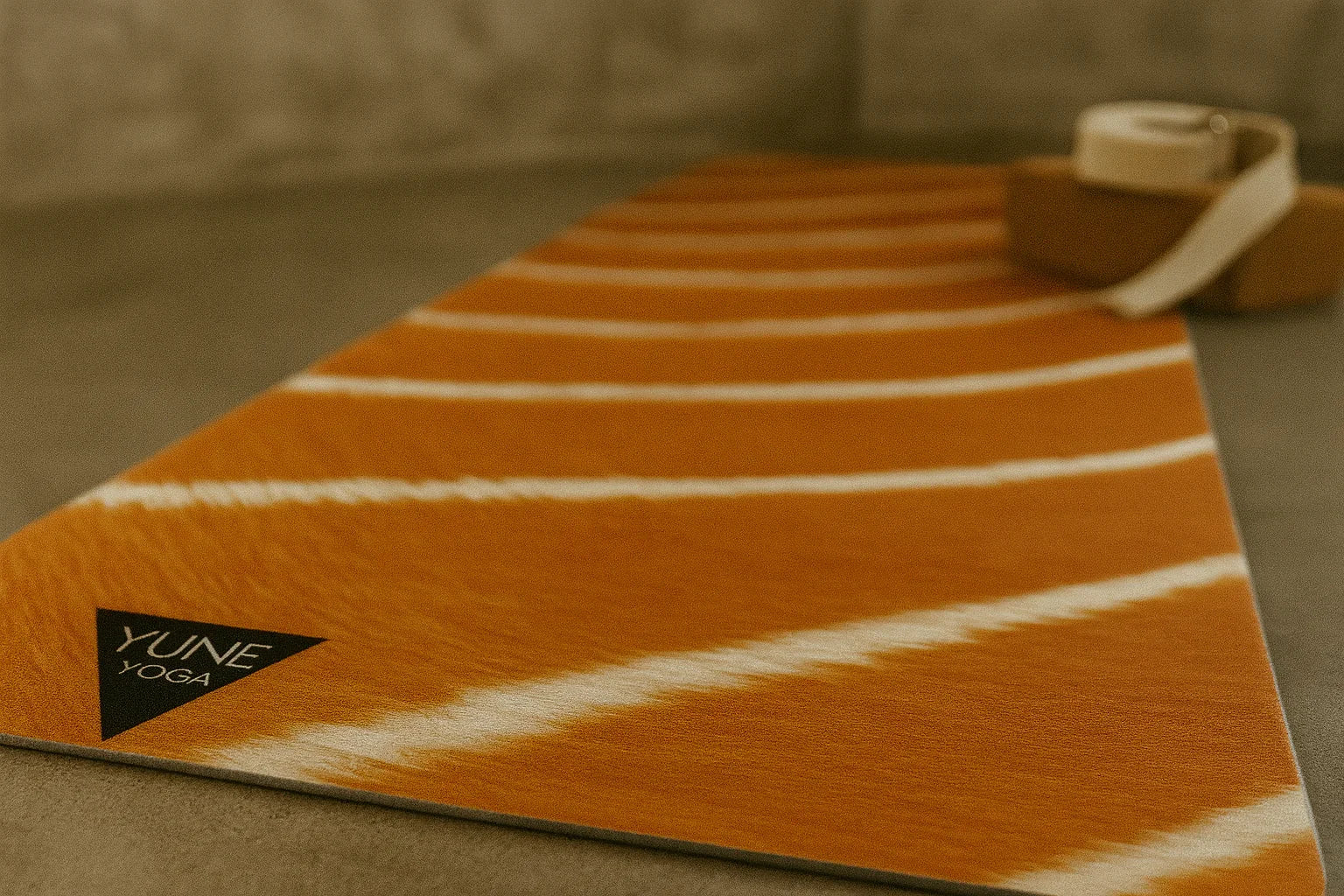 Orange and white striped yoga mat with 'Yune Yoga' logo on a neutral background