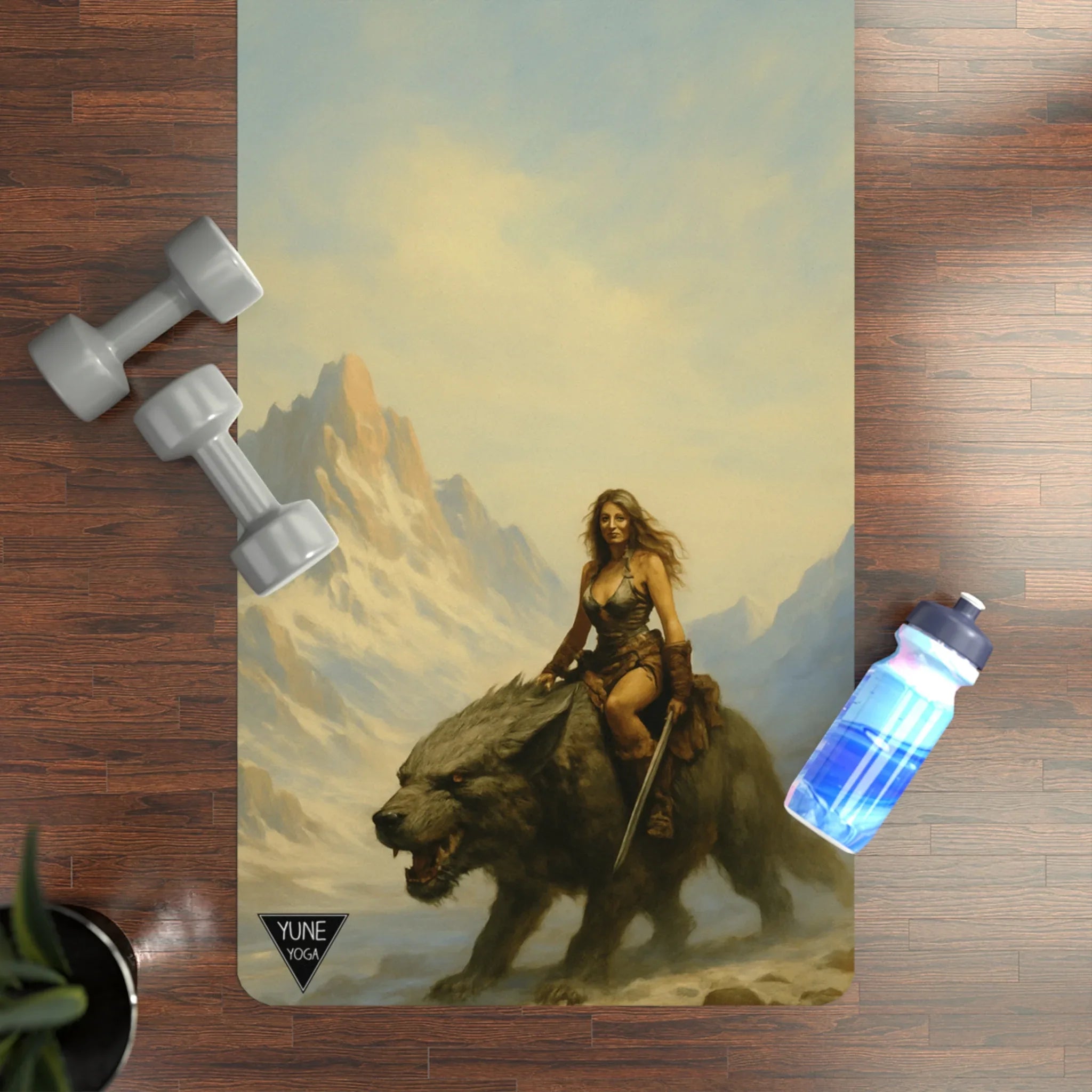 Yoga mat with fantasy design of a woman riding a bear, placed on a wooden floor with dumbbells and a water bottle.
