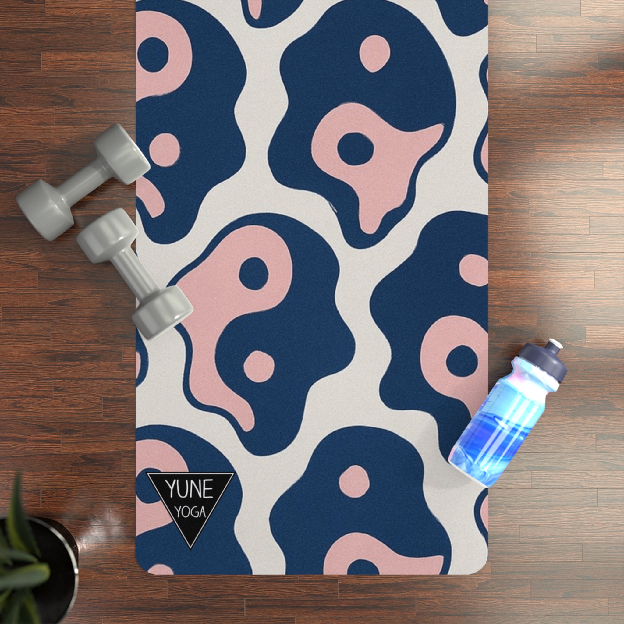 YUNE yoga mat with blue and pink abstract design on a wooden floor with dumbbells and a water bottle.