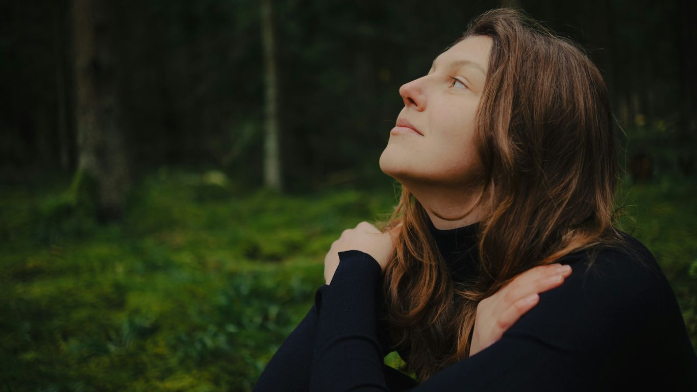 Woman with eyes closed embracing herself in forest