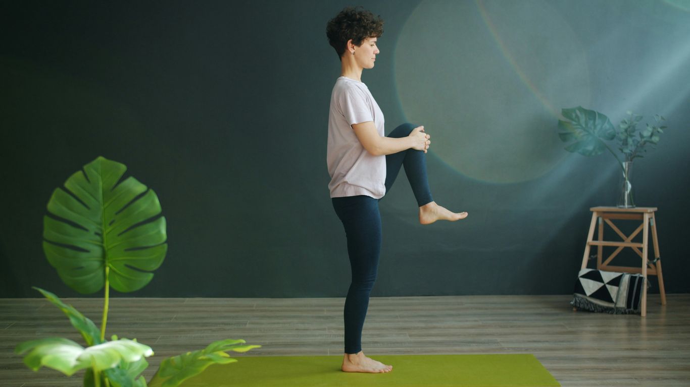 Woman practicing yoga on a green mat indoors.