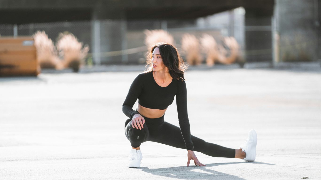 woman in black tank top and black leggings holding black and white nike shoes