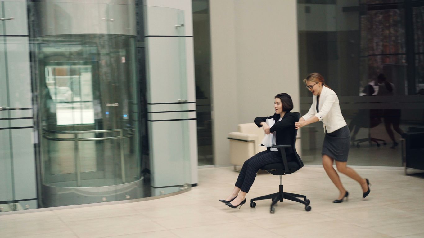 Two women pushing chair near glass elevator