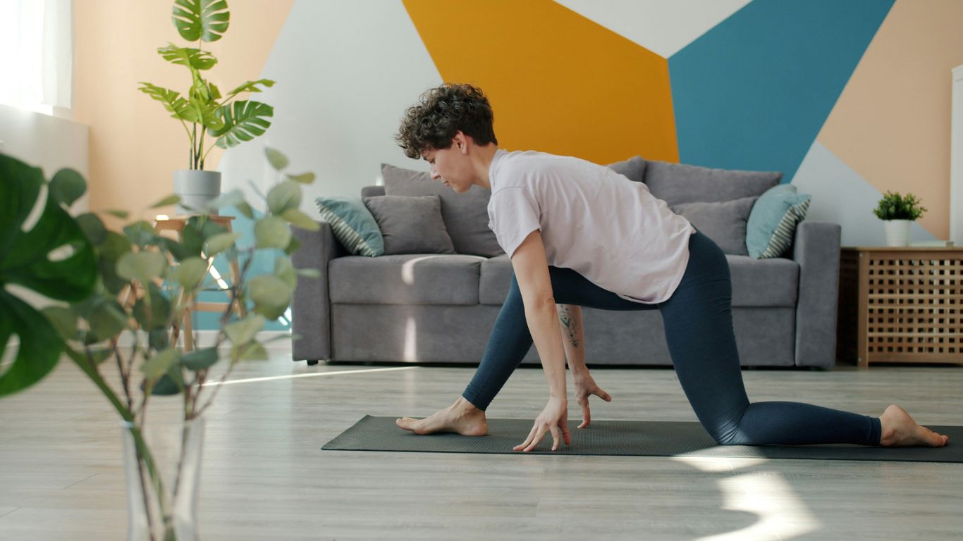 Woman doing yoga on a mat in a living room.