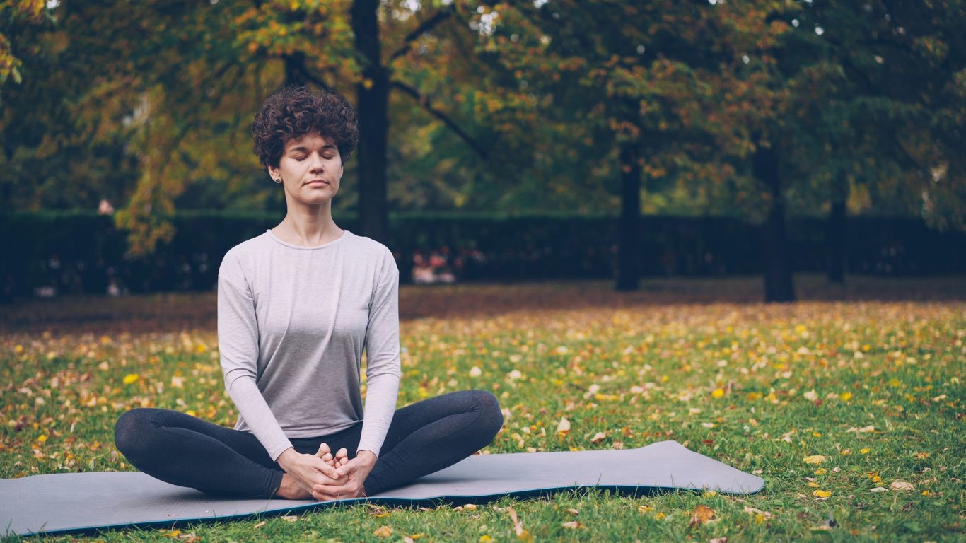 Woman meditating in a park on an autumn day.