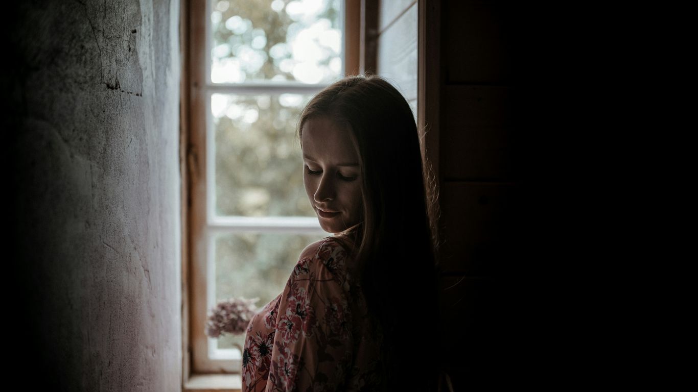 woman in red and white floral dress standing beside window