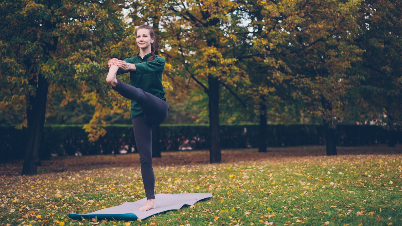 Woman practicing yoga on mat in autumn park