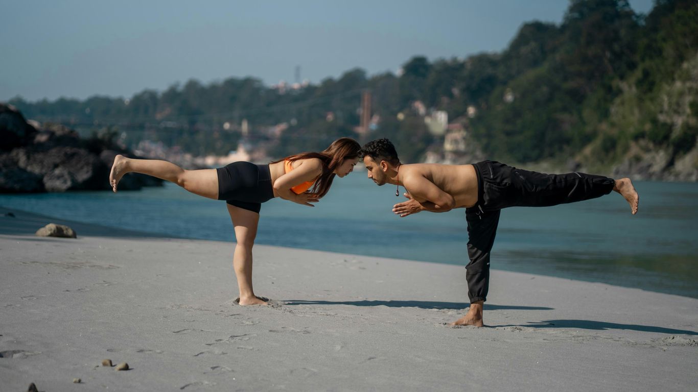 Couple doing yoga on a sandy beach by the water.