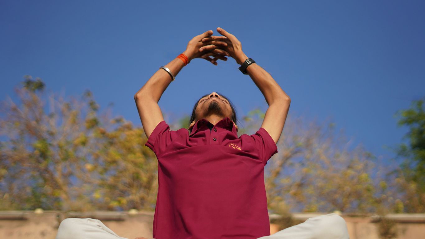Man practices yoga outdoors on a bright, sunny day.