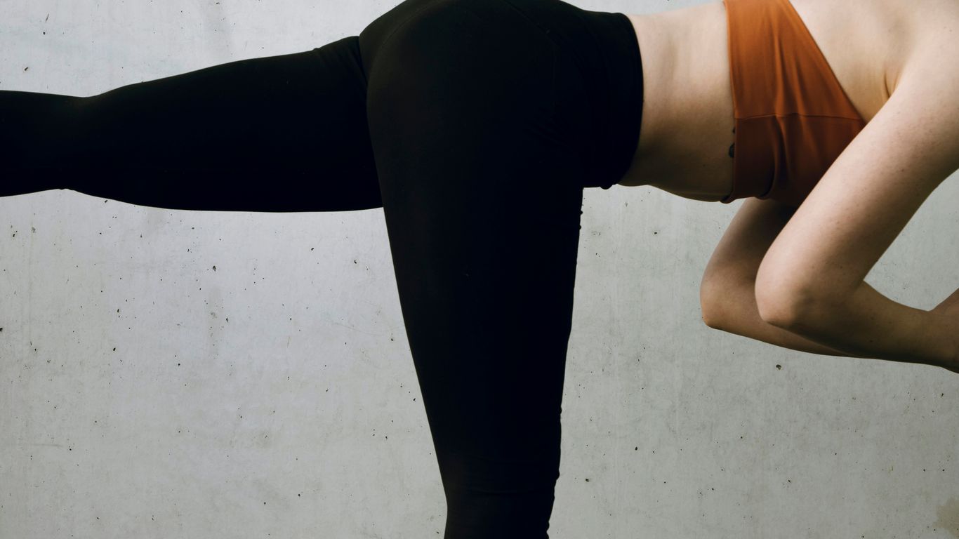 a woman in black and orange is doing a yoga pose