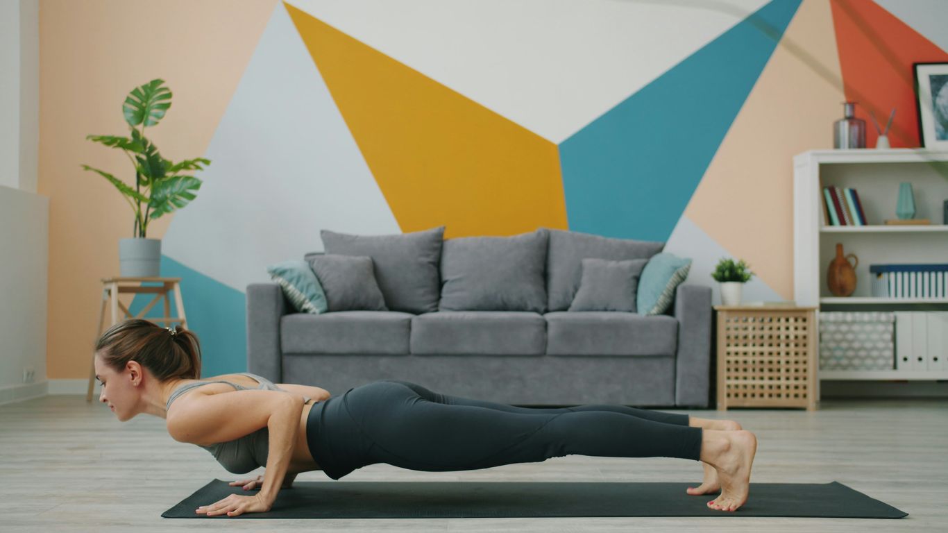 Woman doing a push-up on a yoga mat indoors.