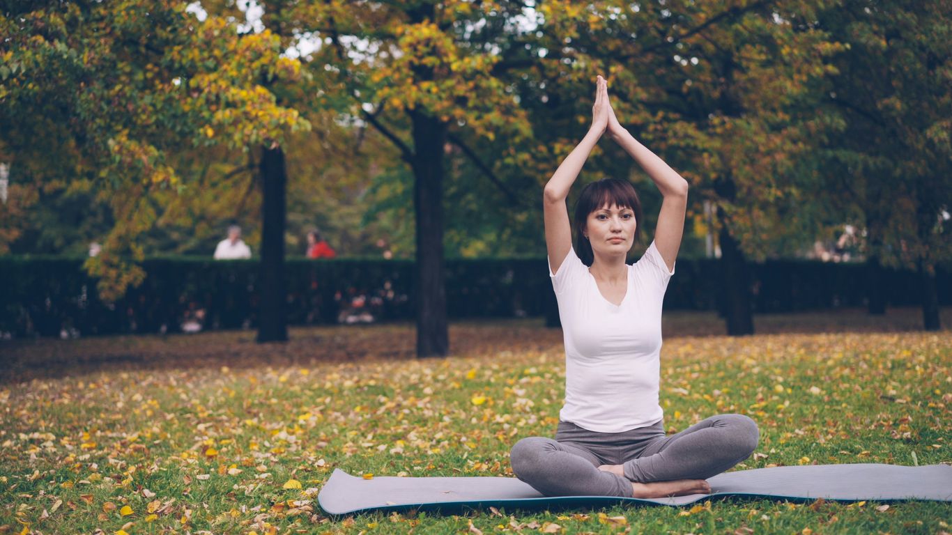 Woman meditating in a park with autumn trees.