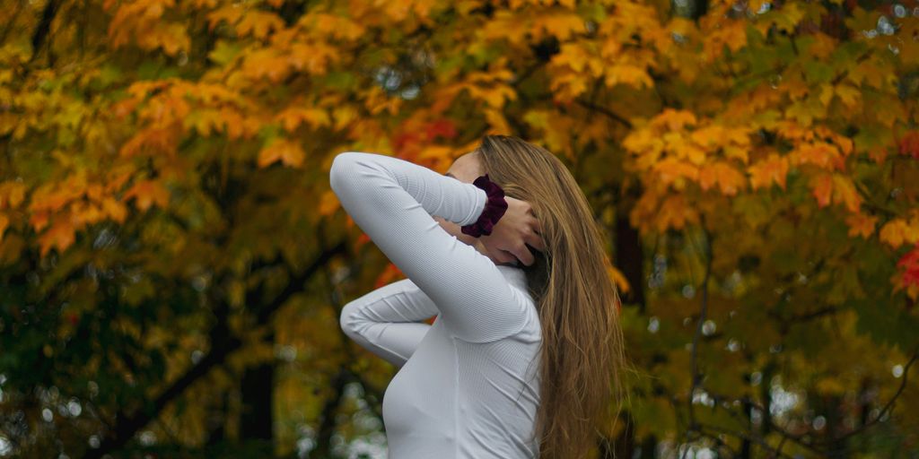 woman in white long sleeve shirt and white pants standing near yellow leaf trees during daytime