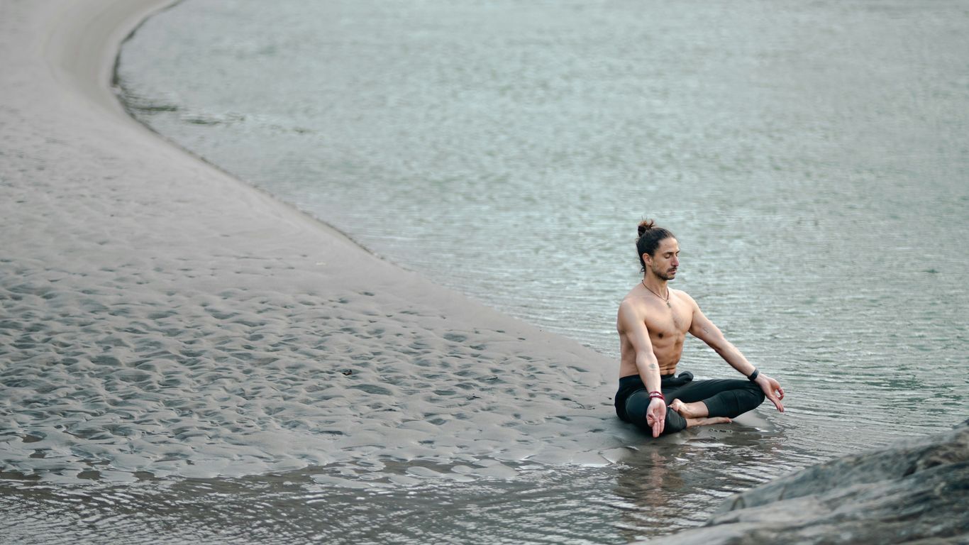 a shirtless man sitting on the edge of a body of water